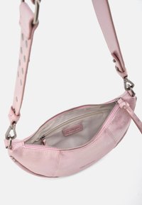 Sac en cuir rose de forme incurvée, doté d'une fermeture éclair et d'un intérieur doublé. La bandoulière présente des détails découpés et des accents en métal argenté.