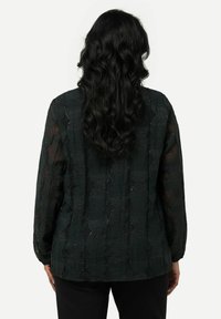 Blusa nera con texture che presenta un motivo a strati, maniche lunghe e una vestibilità rilassata. Il tessuto trasparente esalta i dettagli del design.