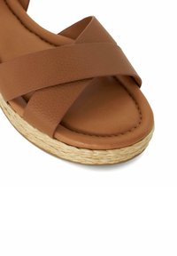 Brown sandal with crisscross leather straps and a braided straw platform sole on a white background.