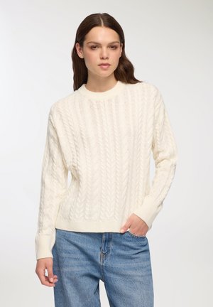 Maglione a trecce di colore avorio, con collo rotondo e polsini a costine. Abbinato a jeans in denim azzurri per un look casual.