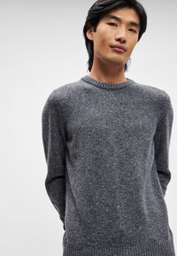 Pulover tricotat gri cu decolteu rotund, având un model texturat. Material moale și manșete și tiv din țesătură rib dobândesc o ajustare confortabilă.