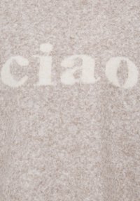 Tissu beige doux avec le mot "ciao" écrit en lettres blanches duveteuses à la surface.