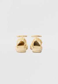 Sandales espadrilles tissées jaunes avec un design découpé, une bride à la cheville et une semelle en jute naturel. Ouverture à l'arrière et bout rond. Fini texturé.