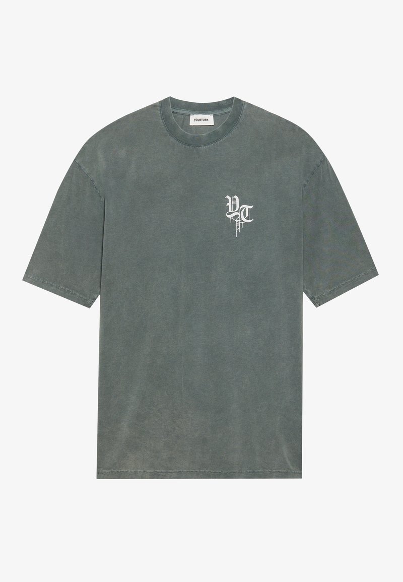 Dunkelgrünes, oversized Baumwoll-T-Shirt mit rundem Halsausschnitt und kurzen Ärmeln. Mit einem weißen Grafik-Logo auf der linken Brust.