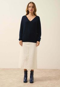 Granatowy sweter w serek wykonany z miękkiej dzianiny, zestawiony z białą midi spódnicą z denimu z widocznym przeszyciem oraz niebieskimi botkami na kostkę z grubym obcasem.