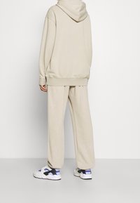 Beige hoodie and matching sweatpants made of soft material; relaxed fit with ribbed cuffs and a drawstring hood. Sneakers with black and blue accents.