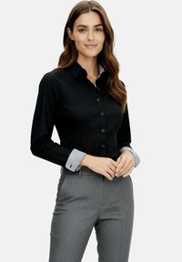 Black button-up shirt with a structured design, featuring a striped inner collar and cuffs; paired with gray tailored trousers.