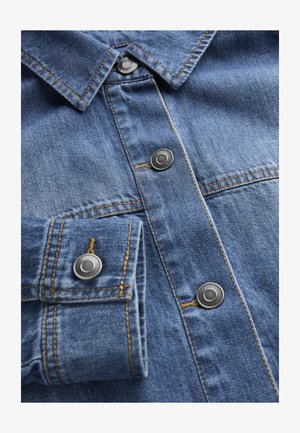 Nahaufnahme eines blauen Jeanshemds mit Kragen, Metall-Druckknöpfen, Manschette mit Knopf und orangefarbenen Nähten.