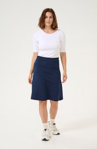 Navyblaue Rock mit einem ausgestellten Design, aus weichem Material gefertigt. Kombiniert mit einem enganliegenden weißen T-Shirt und neutralfarbigen Turnschuhen.