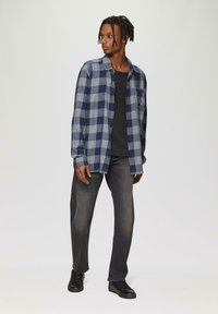 Niebieska i szara koszula w kratę z zapinaniem na guziki, noszona na czarnej koszulce, w połączeniu z ciemnoszarymi dżinsami i czarnymi butami.