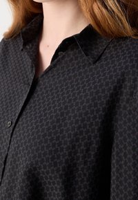 Zbliżenie na osobę w czarnej koszuli z guzikami, z ciemnoszarym wzorem w kratę houndstooth i klasycznym kołnierzykiem.
