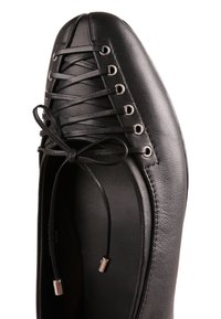 Chaussure en cuir noir à lacets sur le devant, embout rond, œillets métalliques et lacets fins noués en nœud, vue de dessus sur fond blanc.