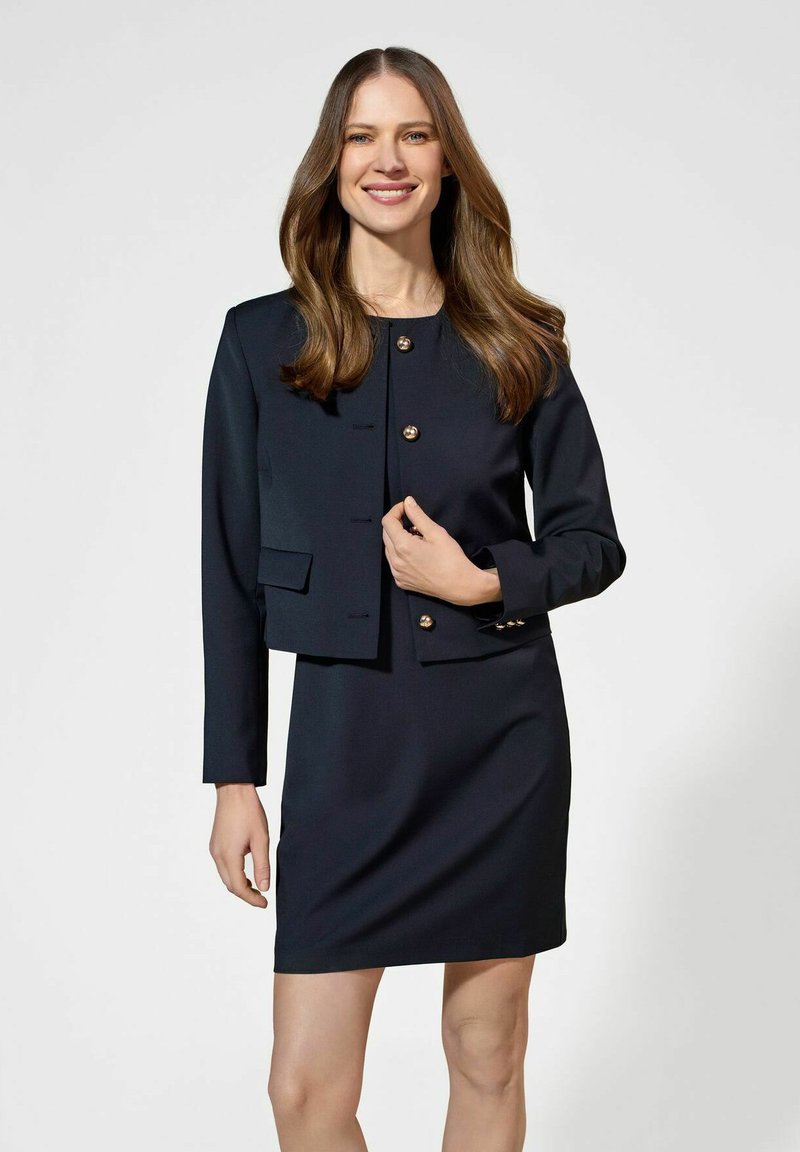 Granatowa marynarka dopasowana z złotymi guzikami oraz dopasowana sukienka do kolan. Gładka faktura z wyraźną konstrukcją i subtelnymi detalami kieszeni.