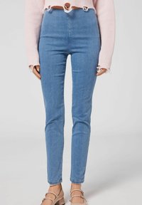 Högmidjade blå denimjeans med slim fit och lätt stretch. Har en fransad fåll och en slät yta. Bärs med en rosa kortärmad tröja.