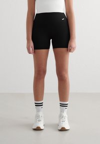 Sorte ribbede shorts med høy midje, parret med hvite joggesko og stripete sokker. Den glatte teksturen og tettsittende formen fremhever komfort.