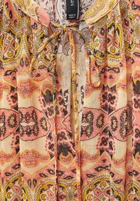 Blusa leggera con stampa floreale e paisley in tonalità di rosa, giallo e marrone; presenta una chiusura con laccetto al collo e tessuto testurizzato.