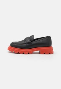 Čierne kožené loafers s červenou masívnou gumovou podrážkou, s okrúhlou špičkou a minimalistickým popruhom na vrchu.