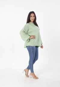 Hellgrüner, übergroßer Strickpullover mit langen Ärmeln, kombiniert mit dunkelblauen Skinny-Jeans und transparenten, absatzhohen Sandalen.