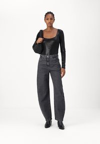 Body lungo nero a maniche lunghe, jeans neri sbiaditi a vita alta e una borsa a tracolla nera con texture. La modella indossa stivali neri con tacco. Sfondo neutro.