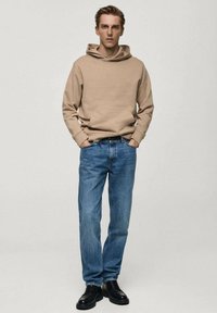 Bež hoodie s kengurufrontim džepom, uparen s svijetloplavim trapericama. Crne cipele upotpunjuju ležeran izgled. Jednostavan, opušten kroj.