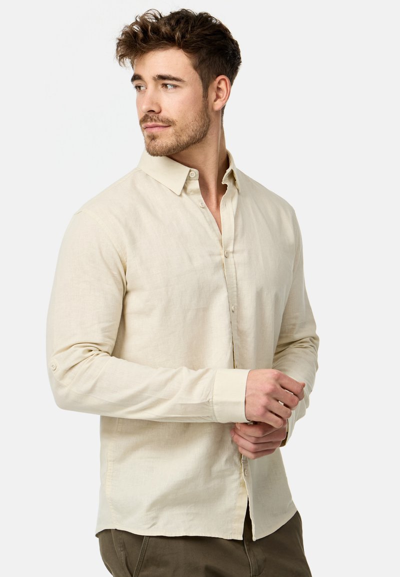 Chemise boutonnée en lin beige clair avec un col classique, des manches longues et une coupe décontractée. Présente une texture lisse et des boutons à l'avant.