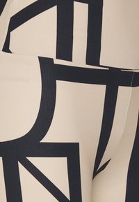 Bežinės legging'ų kelnės su ryškiais juodais geometriniais raštais. Lygus audinys, prigludusi forma ir matomi siuvimo detalės palei siūles.