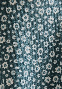 Teal tyg med en strukturerad, ribbad design som har ett vitt blommigt och cirkulärt mönster överallt.