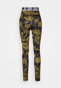 Schwarze Leggings mit einem aufwendigen goldenen Barockmuster. Elastischer Bund mit weißem Branding. Das Material scheint dehnbar und figurbetont zu sein.