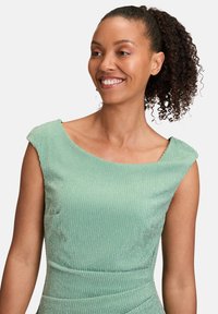 Robe vert menthe avec un design texturé et côtelé. Présente un décolleté arrondi et une silhouette ajustée. Manches courtes à capuche.