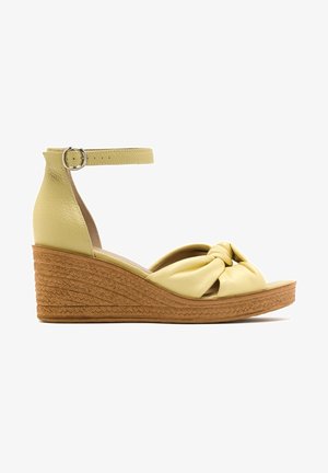 Sandale compensée en cuir jaune avec bride avant nouée, bride de cheville avec boucle argentée et semelle plateforme marron texturée.