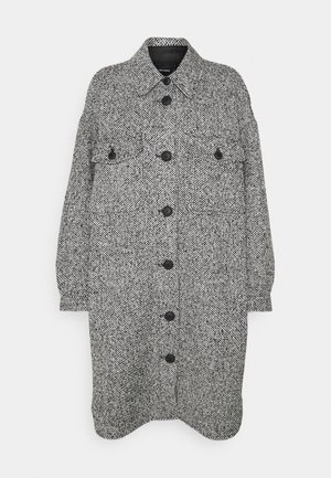 Mustat ja valkoiset teksturoidut takki, jossa on kaulus, etupainon suljenta, kaksi tasku-yläruutua ja pitkät hihat. Kankaan kuvio on houndstooth.