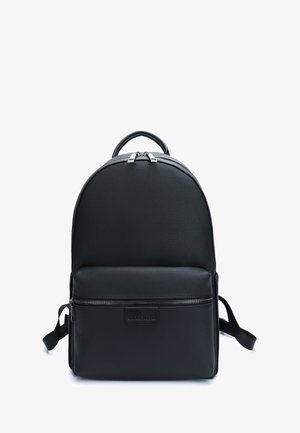 Sac à dos en cuir noir avec un haut arrondi, une poche zippée à l'avant et des bretelles réglables. Il présente une surface texturée et des accents de zipper métalliques.