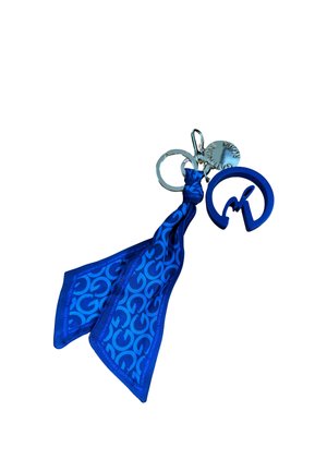 Portachiavi con tessuto blu a motivo annodato e un ciondolo circolare con logo blu attaccato a due anelli metallici e una piccola targhetta rotonda in metallo.
