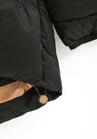 Czarna kurtka puchowa o błyszczącej fakturze, z złotym wnętrzem, z logo na sznurków ściągających oraz widocznymi detalami przeszycia.