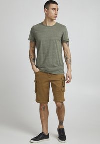 Olive green short-sleeve t-shirt with crew neck, paired with brown cargo shorts featuring side pockets. Black sneakers complete the outfit.