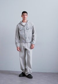 Lysegrå denimjakke med lommer og hætte, parret med matchende lysegrå bukser og sorte sko. Glat tekstur og afslappet pasform.