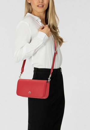 Rode leren crossbodytas met een gladde textuur, rechthoekige vorm en zilveren hardware. Verstelbare riem bevestigd.