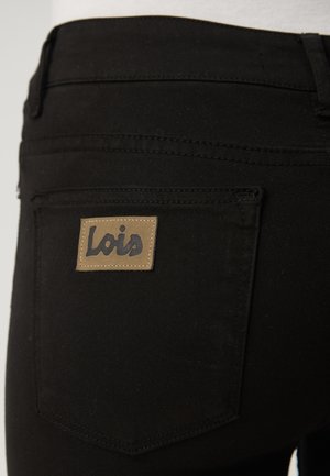 Black jeans with a textured finish, featuring a rectangular brown leather patch with the word "Lois" in black lettering.
