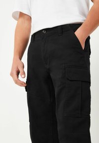 Schwarze Cargo-Hosen mit mehreren Taschen, Knopfverschluss und geradem Bein, aus strapazierfähigem Baumwollstoff. Texturierte Oberfläche.