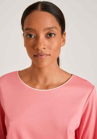 Roze langmouwen top met een gladde textuur en een ronde halslijn, voorzien van een contrasterende witte bies. Eenvoudig ontwerp zonder patronen of accenten.