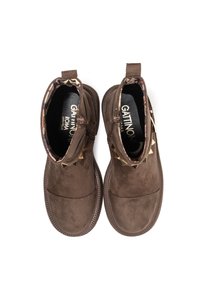 Botines de ante marrón con un acabado texturizado, que presentan tachuelas metálicas en la parte superior y un forro interior con un patrón. Cierre con cremallera en el lateral.