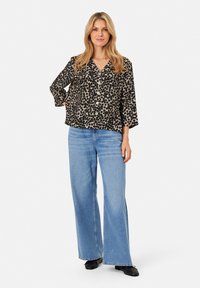 Blusa a pois neri e beige con scollatura a V e maniche a tre quarti, abbinata a jeans a gamba larga blu chiaro e scarpe nere.