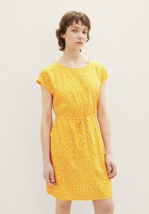 Robe jaune en tissu léger, avec un col rond, des manches courtes et un motif floral blanc, cintrée à la taille.