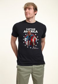 Camiseta de algodón negra con un gráfico del Capitán América rodeado de estrellas. Presenta texto en negrita y colores vibrantes en el diseño.