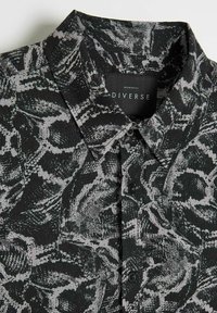 Czarna koszula wykonana z fakturowanej tkaniny z szarym abstrakcyjnym wzorem, zapinana na guziki i posiadająca kołnierzyk. Metka głosi "Diverse."