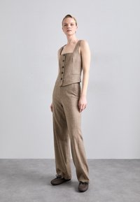 Καφέ εφαρμοστό αμάνικο τοπ με τετράγωνη λαιμόκοψη και μαύρα κουμπιά, συνδυασμένο με αντίστοιχες φαρδιές παντελόνες από υφασμάτινη υφή.