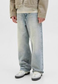 Jean en denim délavé avec une coupe ample, présentant un léger effet dégradé et une coupe droite. Associés à des baskets blanches avec des accents gris.