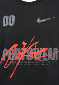 Črna bombažna majica s širokim sivim napisom "00" in "SPORTSWEAR", poudarjenim z rdečo barvno kapljico, v bližini logotipa Nike.