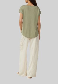 Oliwkowy top z krótkim rękawem o zaokrąglonym dole, w połączeniu z luźnymi, kremowymi spodniami o szerokich nogawkach z bocznymi kieszeniami. Gładka tekstura materiału.