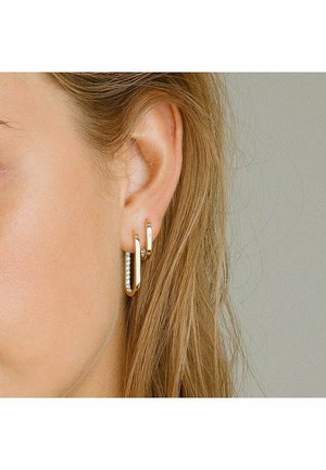Guldörhängen i hoop-modell med en glänsande yta, som har en liten sektion prydd med klara rhinestones för extra detalj och textur.